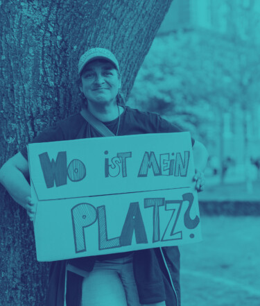 Anni hält ein Schild in der Hand mit der Aufschrift: Wo ist mein Platz?