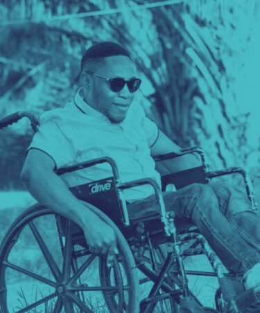 Ein Schwarzer Mann sitzt im Rollstuhl und hat eine Sonnenbrille auf während er lächelt