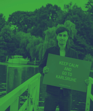 Bijan Moini hält ein Schild mit dem Schriftzug "Keep calm and go to Karlsruhe"